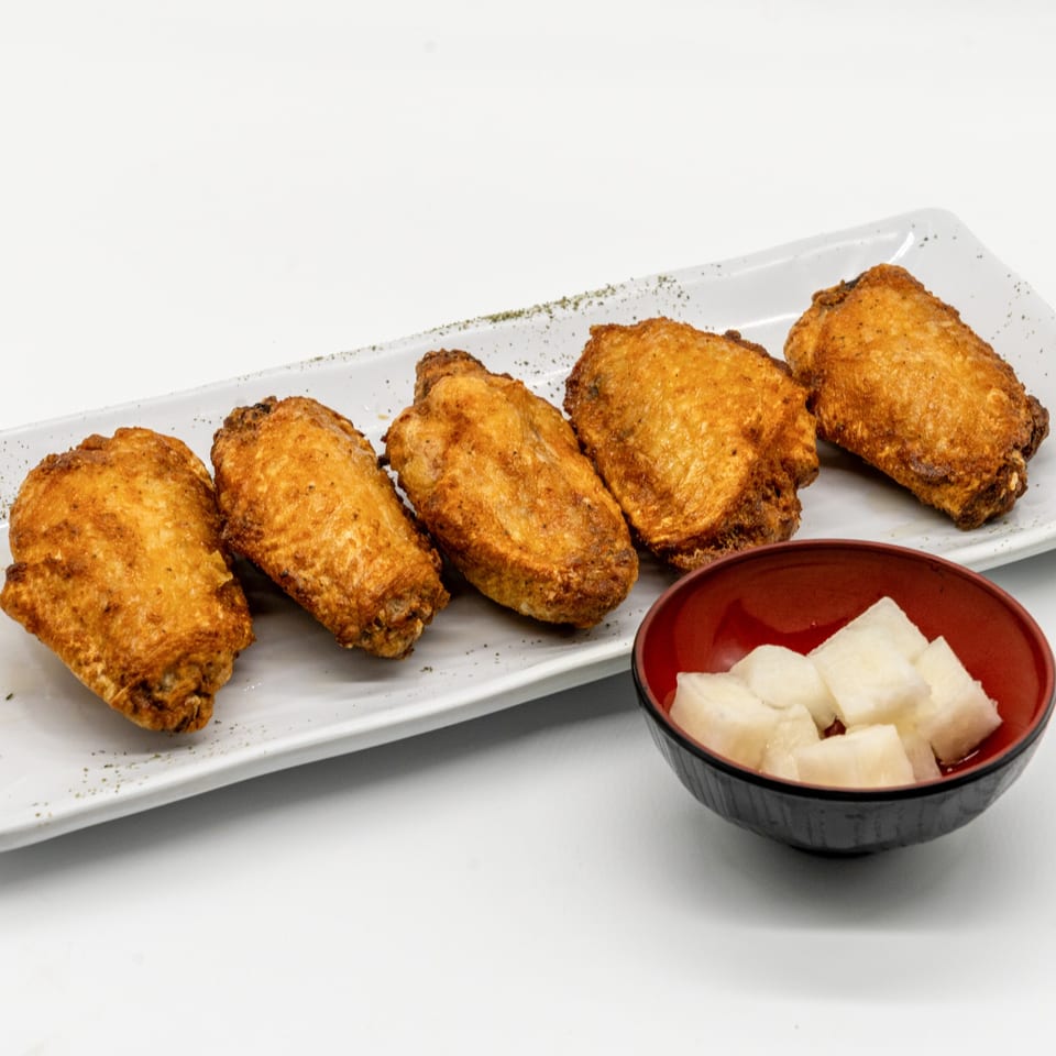 Five crispy fried chicken wings on a white plate with a side of pickled daikon radish.