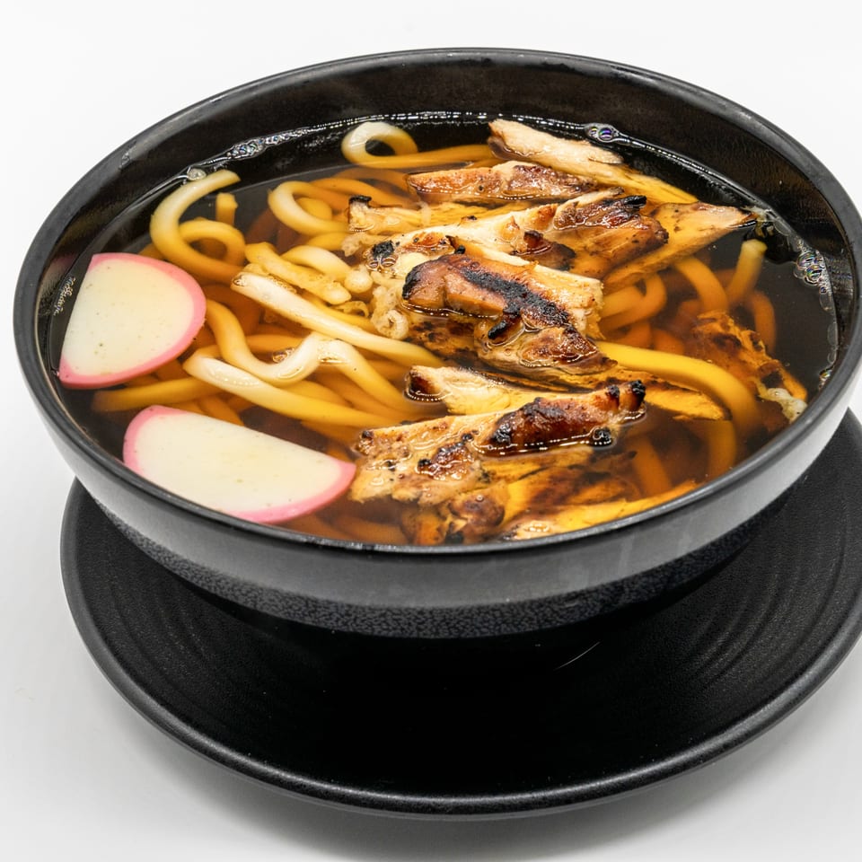 A black bowl of JooN's Sushi udon soup with grilled chicken and fish cakes.