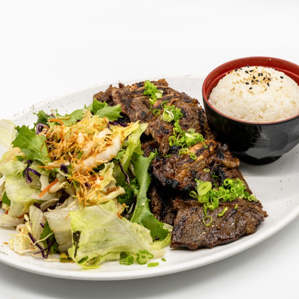 Grilled short ribs with green onions, a fresh salad, and a bowl of white rice with sesame seeds.