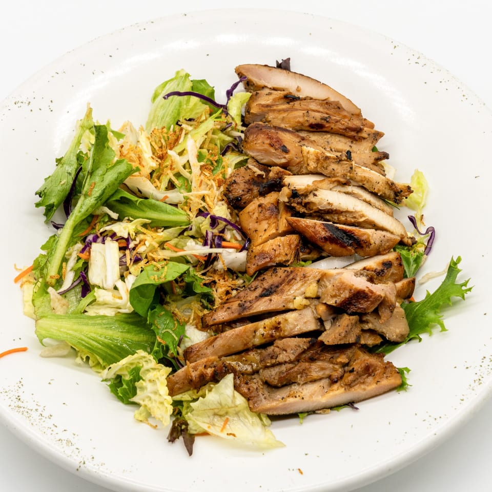 Grilled chicken slices and fresh green salad with crispy toppings on a white plate.