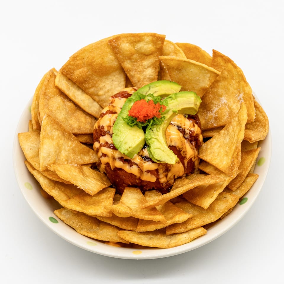 Sushi nachos with a mound of spicy tuna, avocado slices, and orange tobiko, surrounded by crispy chips.
