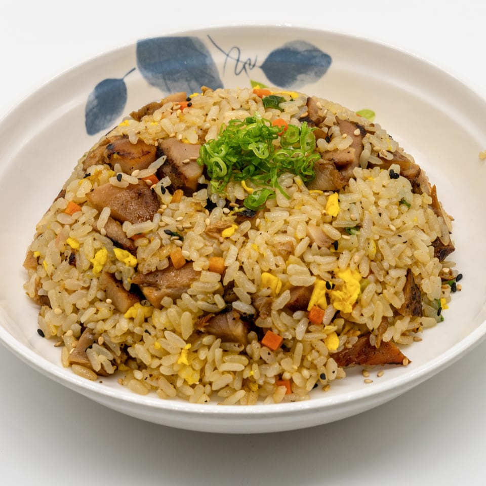 A close-up of chicken fried rice with chopped scallions, carrots, and scrambled egg in a white bowl.