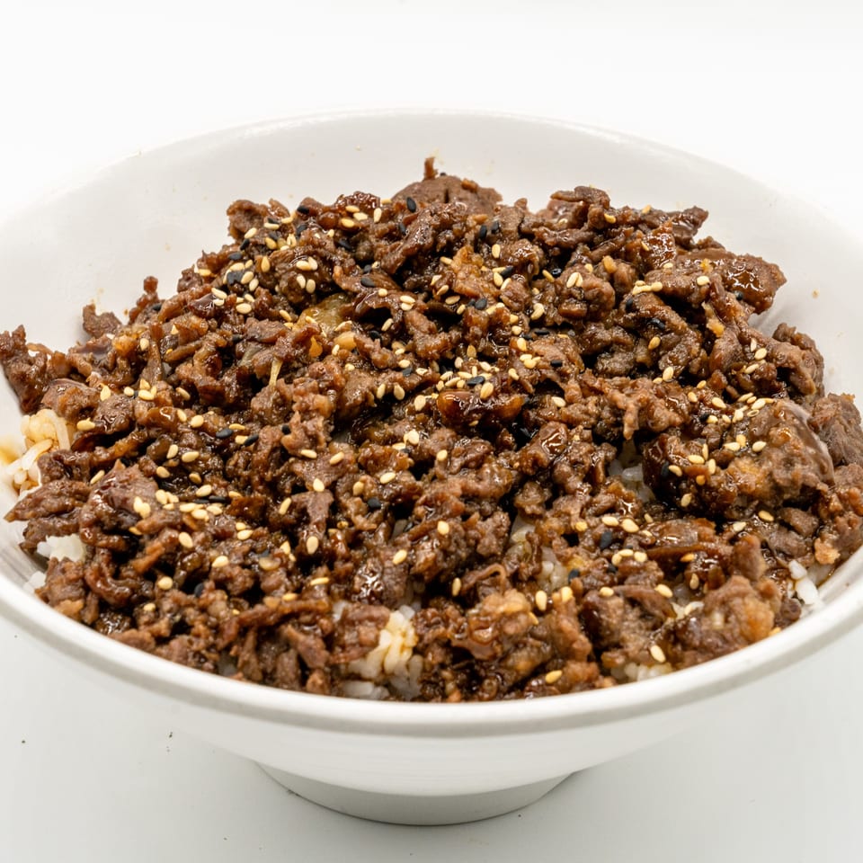 A white bowl filled with JooN's Sushi's beef gyudon, topped with sesame seeds.